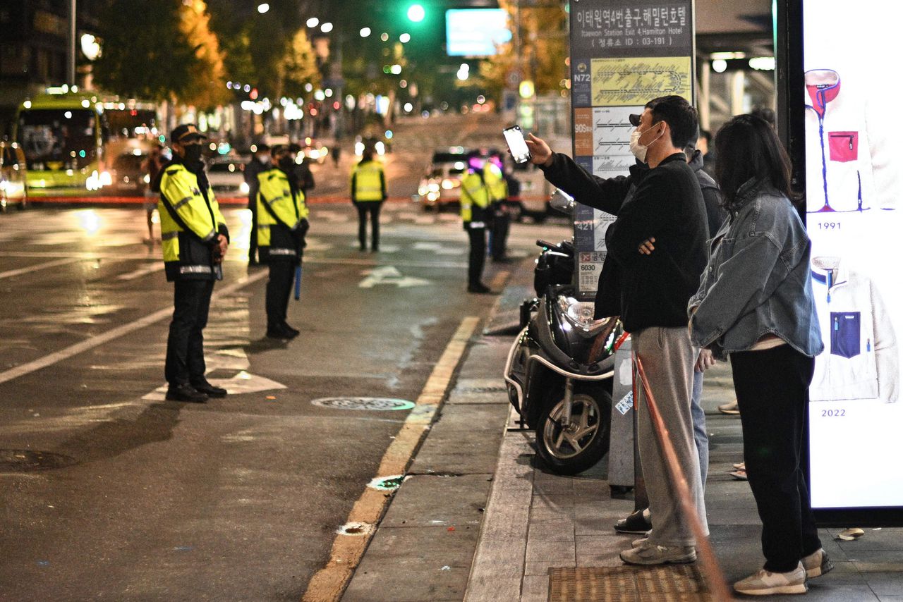 De politie houdt de wacht terwijl toeschouwers achter een lint staan ​​rond de plaats van de Halloween-stormloop in het district Itaewon in Seoul.