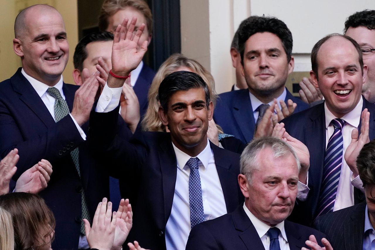 Rishi Sunak (midden), de nieuwe partijleider van de Britse Conservatieven en daarmee de nieuwe Britse premier, zwaait maandag voor het hoofdkwartier van de Conservatieve Partij in Londen.