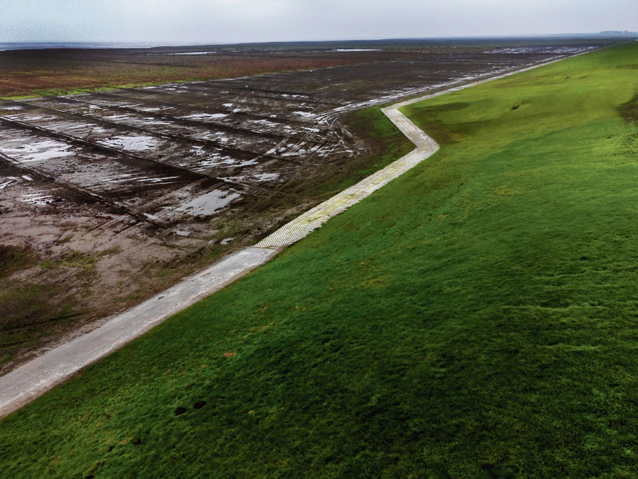 De brede groene dijk is gemaakt van materiaal uit de buurt: havenslib, polderslib en kwelderklei. Hij bevat geen asfalt.