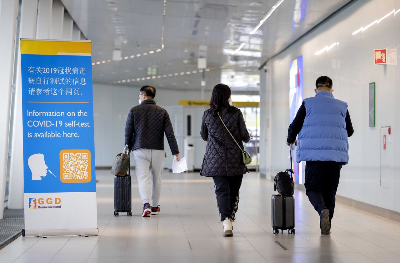 Reizigers uit China lopen langs een banner met informatie over het coronavirus op Schiphol.