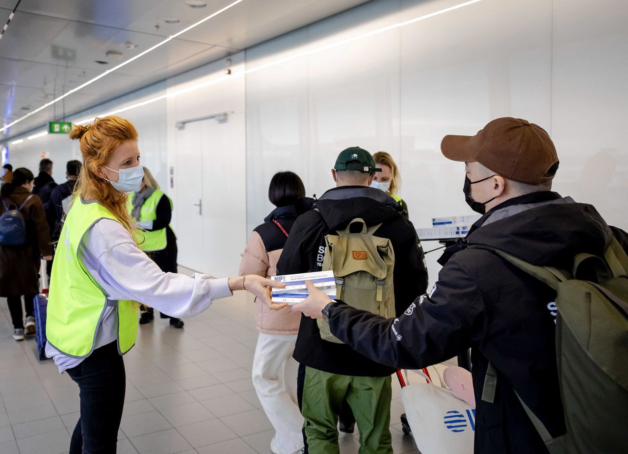 Een medewerker van de GGD deelt op Schiphol gratis coronazelftesten uit onder reizigers uit China.