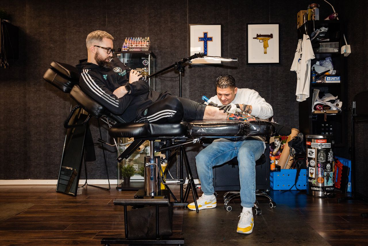 Matthew Luhukay (40), eigenaar van de Black Sword Tattoo Parlour, tatoeëert graffitiletters in het been van Kevin (36).