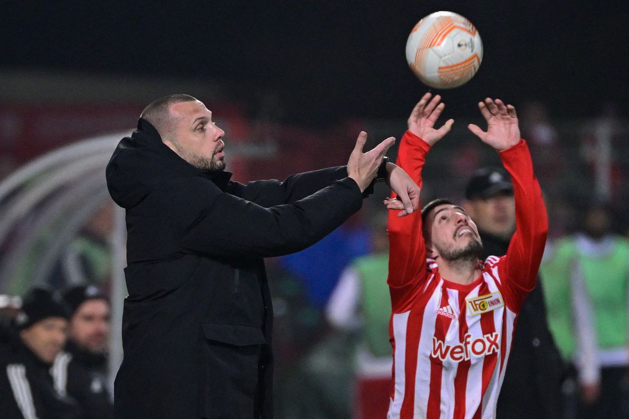 Ajax-coach John Heitinga in gevecht om de bal met Josip Juranovic, speler van Union Berlin.