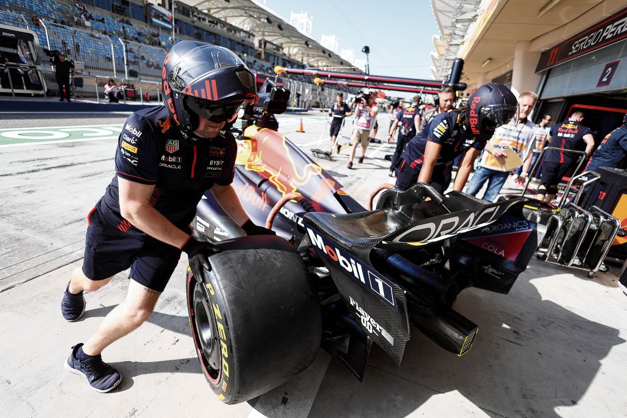 De auto van Max Verstappen wordt in Bahrein door monteurs van Red Bull Racing de garage ingeduwd.