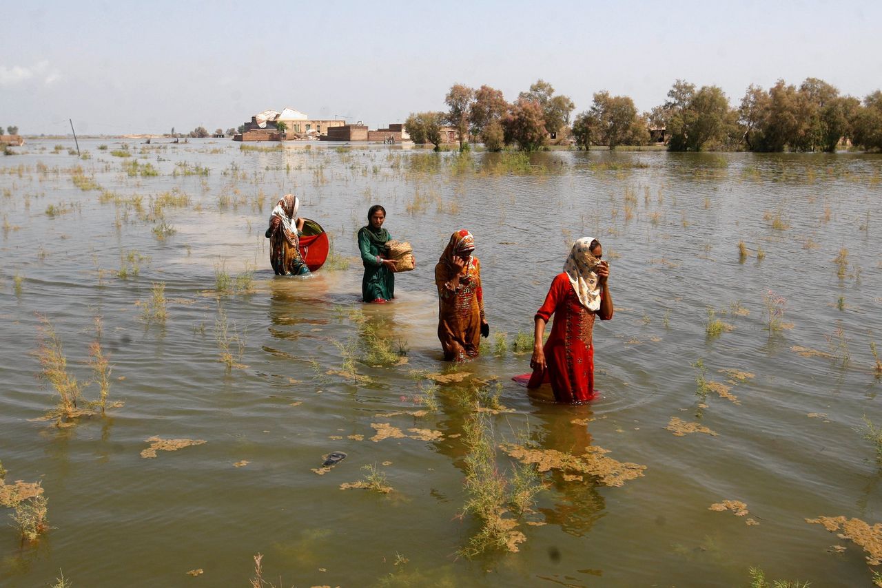 Pakistaanse vrouwen waden door water, op zoek naar een veilige plek.