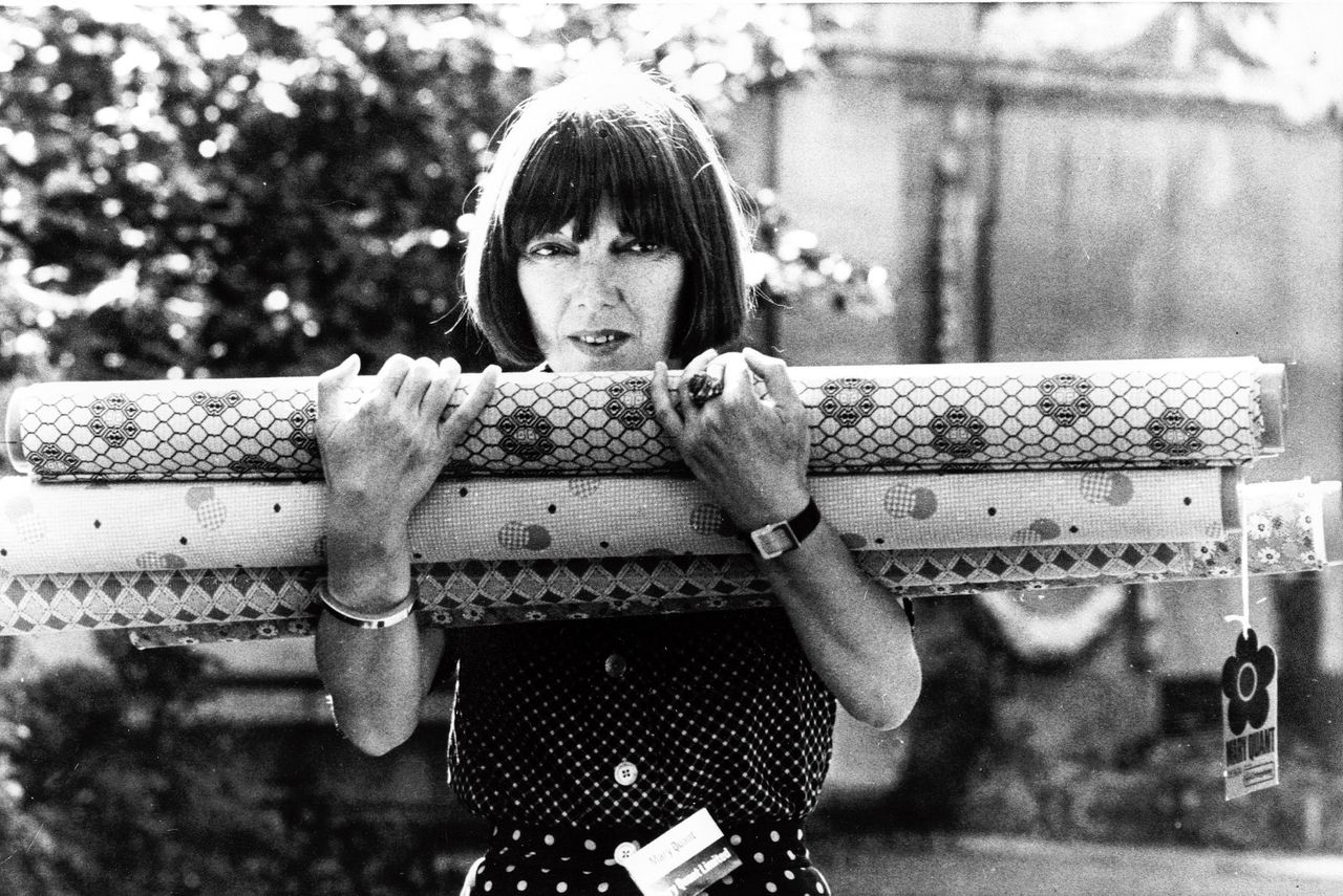 Mary Quant in 1974 met rollen stof. Haar ontwerpen waren revolutionair. In een tijd dat de modehuizen in Parijs peperduur waren, kwam zij met veel goedkopere kleding.