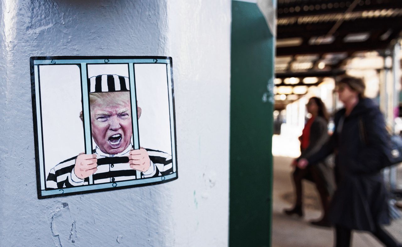 Een sticker van Trump achter tralies is te zien tegenover het gerechtsgebouw in New York. Omdat Trump president was zal hij dinsdag worden begeleid door een gewapend escorte van de Secret Service.