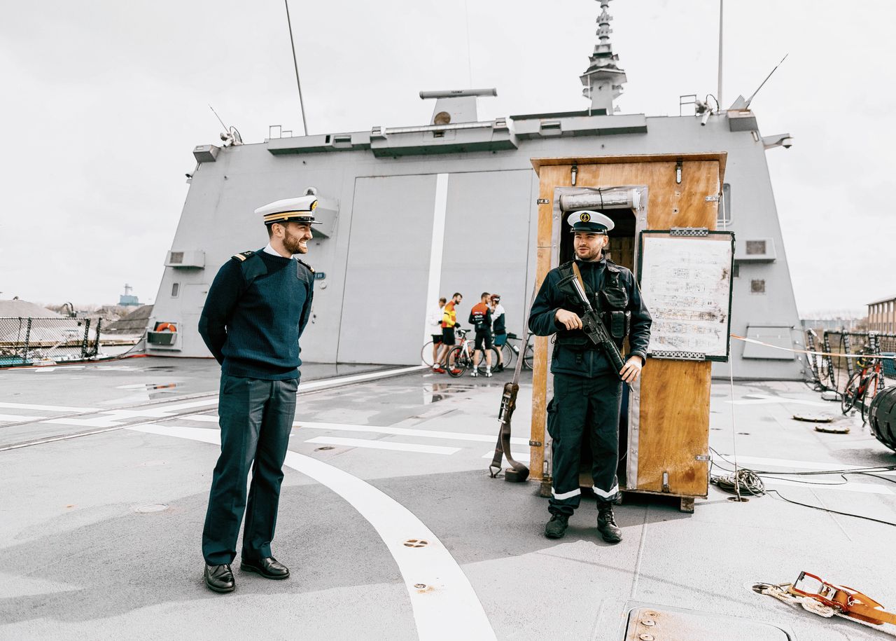 Het Franse oorlogsschip FS Normandie van 142 meter in de Amsterdamse haven ter promotie van een mogelijke duikbootdeal met Nederland. Op de achtergrond de vier bemanningsleden die een rondje gaan fietsen.