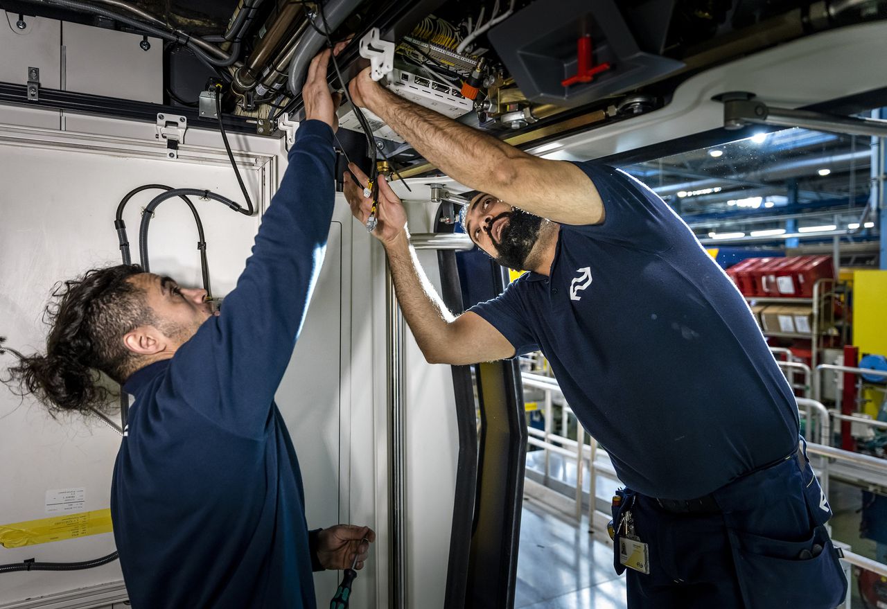 Vluchtelingen werken aan de kabels van een NS-trein.