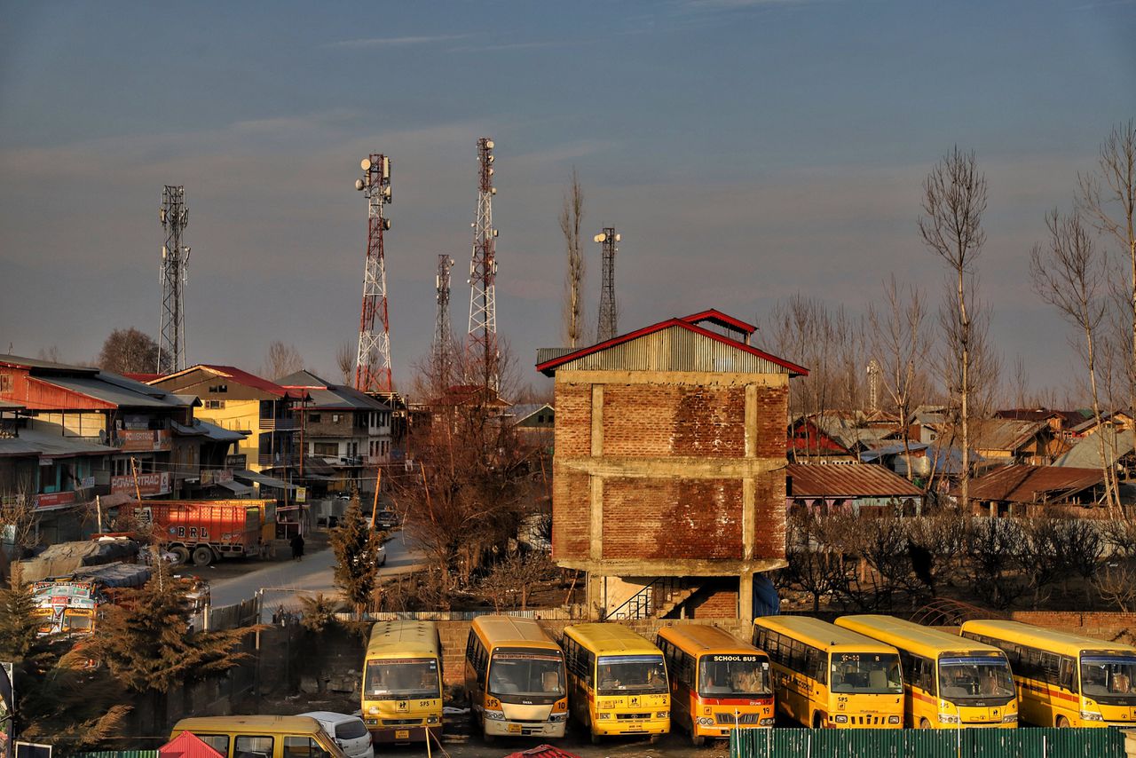 Bussen staan geparkeerd bij een school terwijl torens van mobiele netwerken te zien zijn in de stad Sopore in het noordwestelijke Indiase unieterritorium Jammu en Kasjmir in 2021, kort nadat het 4G-internet er na zeventien maanden hersteld was.