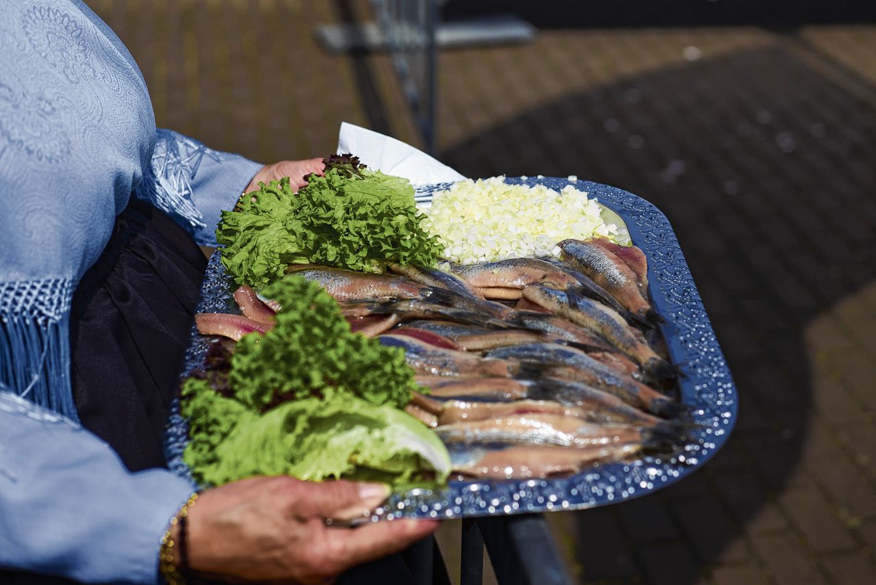 Een schaal met Hollandse Nieuwe, vastgehouden door een Scheveningse vrouw in klederdracht.