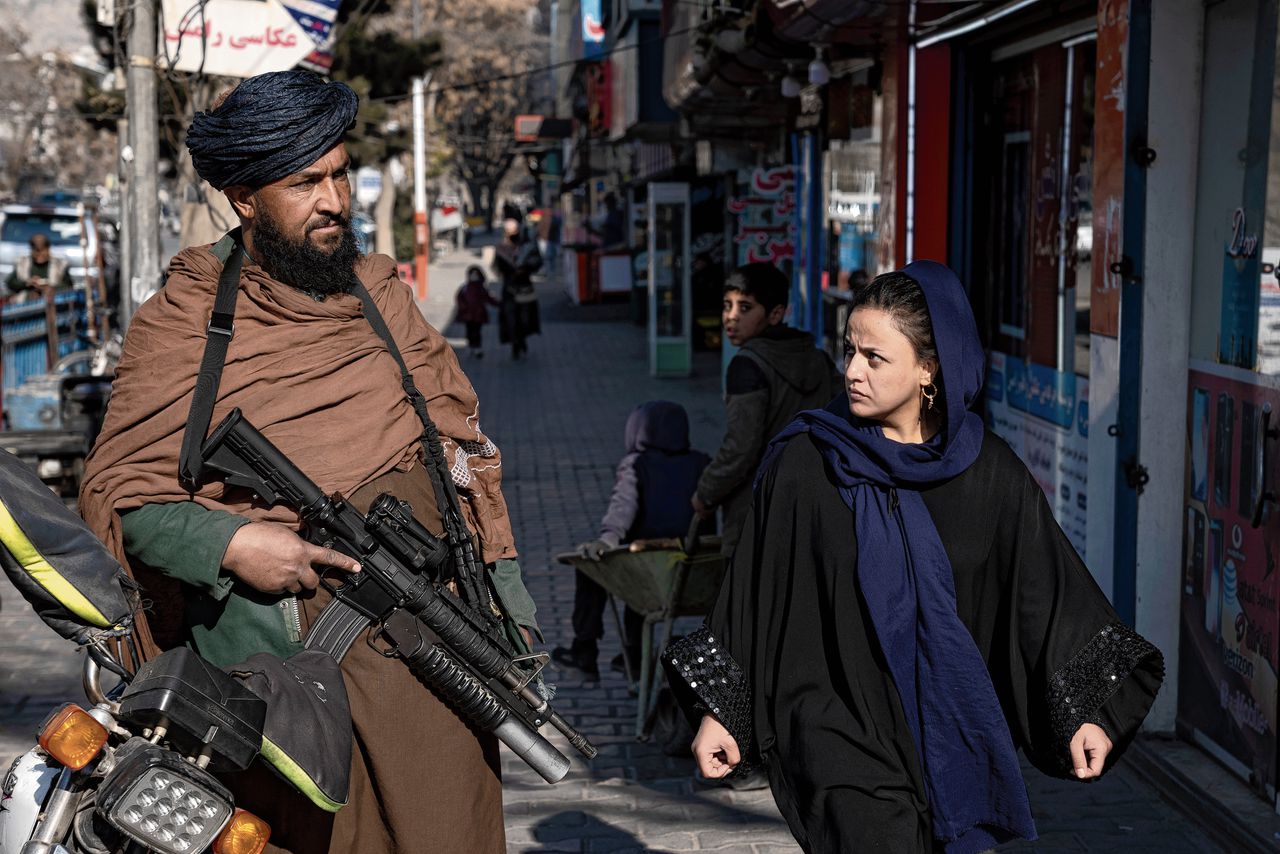 Een vrouw loopt langs een Taliban-strijder die op wacht staat in Kabul, december 2022.