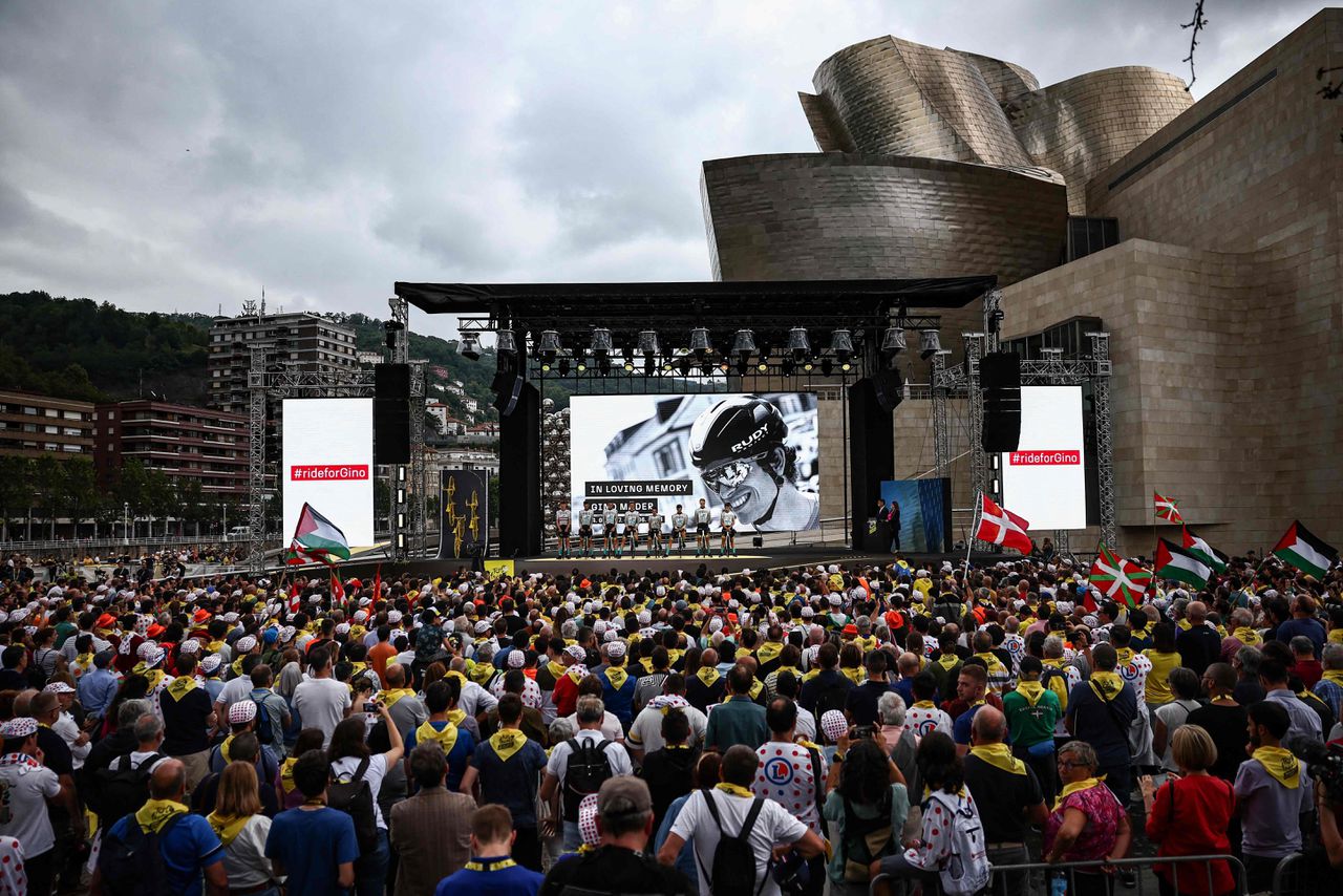 Renners van Bahrain Victorious brengen tijdens de ploegenpresentatie van de Tour de France bij het Guggenheim-museum in Bilbao een eerbetoon aan hun overleden ploeggenoot Gino Mäder, wiens foto op het scherm wordt vertoond.