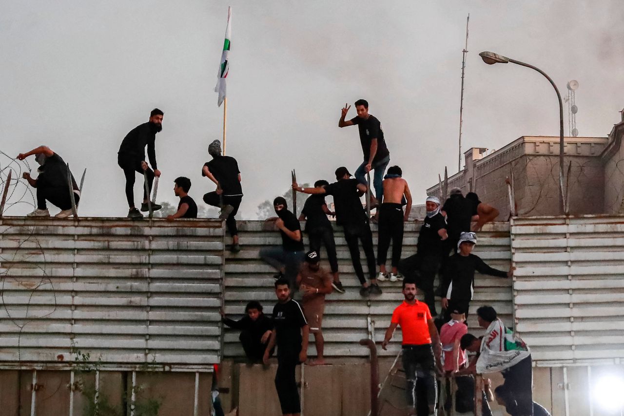 Demonstranten klimmen over hekken van de Zweedse ambassade in Bagdad.