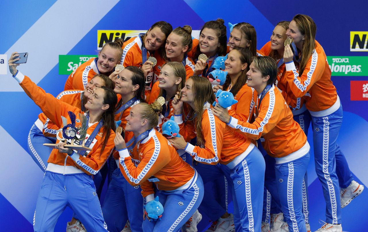 De Nederlandse waterpolovrouwen leggen zichzelf vast met de WK-trofee en hun gouden medailles.