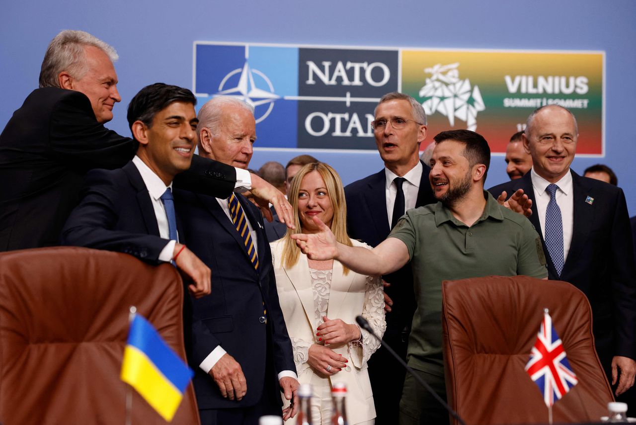 De gastheer in Vilnius, president Nauseda van Litouwen, reikt tussen premier Sunak (VK) en president Biden (VS) door president Zelensky de hand. Premier Meloni (Italië) en NAVO-secretaris-generaal Stoltenberg kijken toe. Helemaal rechts NAVO vicesecretaris-generaal Mircea Geoana.