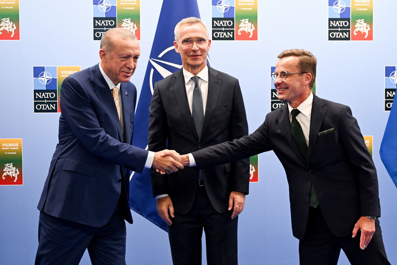 Secretaris-generaal van de NAVO Jens Stoltenberg ziet tevreden toe hoe de Turkse president Erdogan en de Zweede premier Ulf Kristersson elkaar de hand schudden.