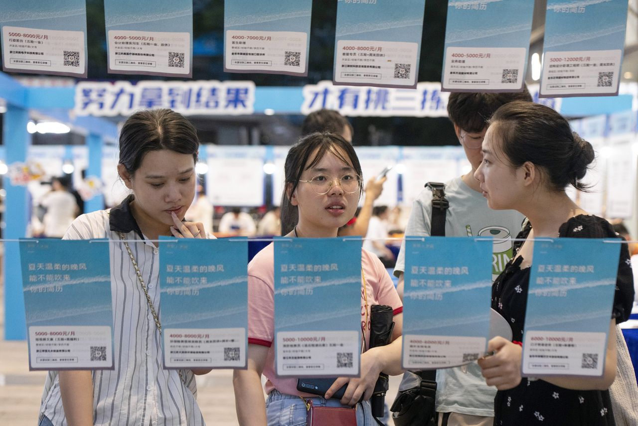 Jonge werkzoekenden lezen posters waarop personeel wordt geworven op een beurs voor afgestudeerden in de oostelijke stad Jinhua.