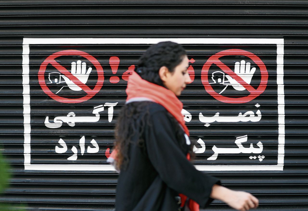 Een vrouw loopt op 10 augustus zonder hoofddoek langs een gesloten winkel in de Iraanse hoofdstad Teheran.