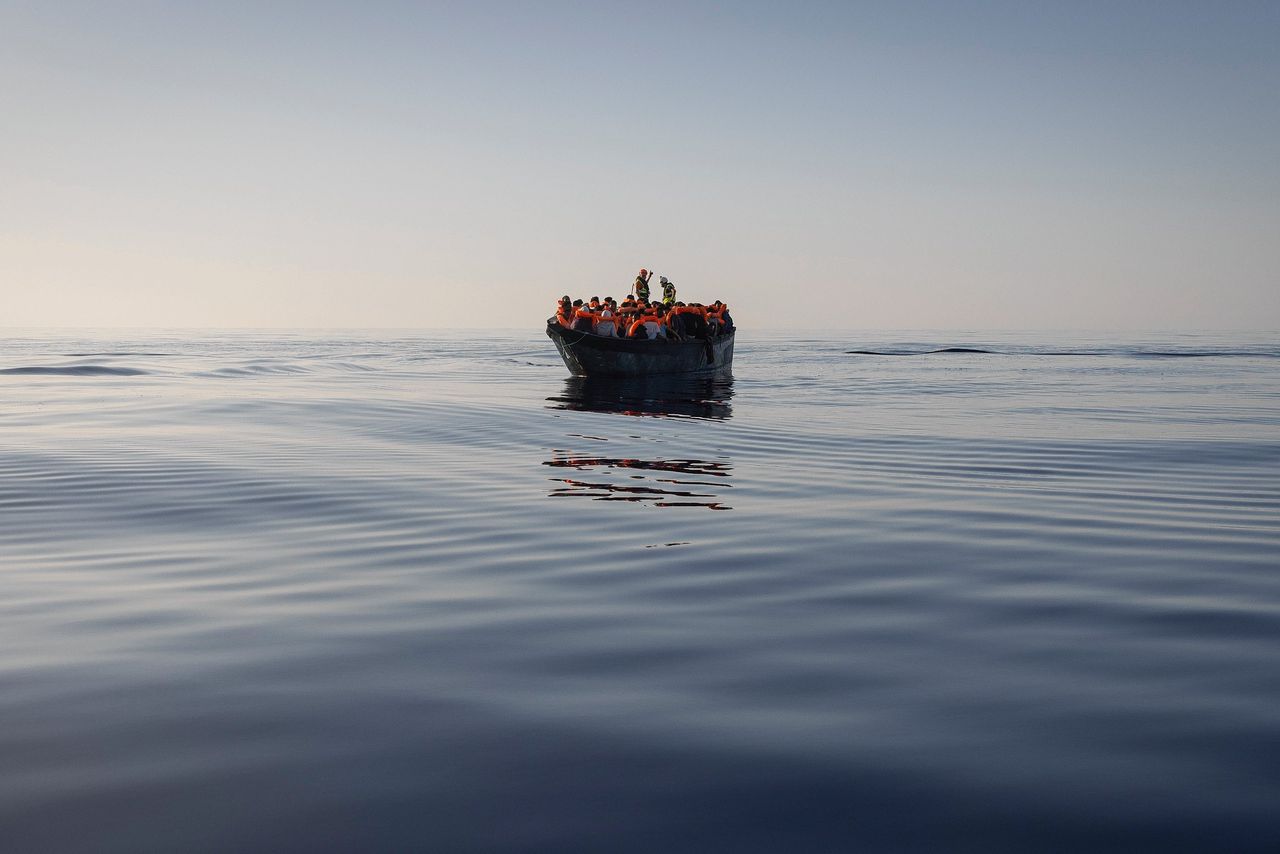 Migranten aan boord van een klein bootje op de Middellandse Zee krijgen reddingsvesten uitgedeeld van vrijwilligers van de ngo’s SOS Mediterranee en het Rode Kruis.