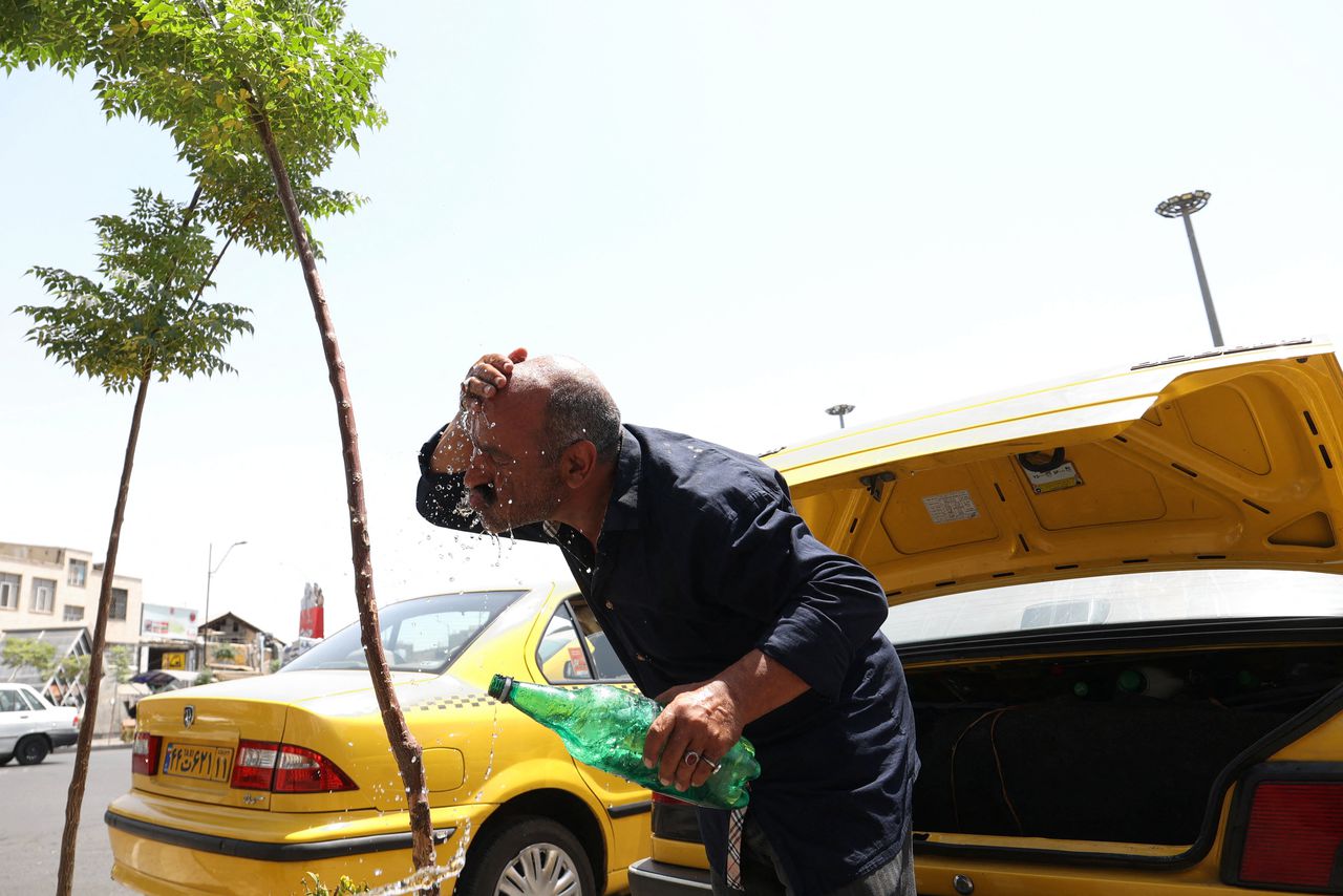 Een Iraanse taxichauffeur koelt zich af met water tijdens de hittegolf in de Iraanse hoofdstad Teheran.