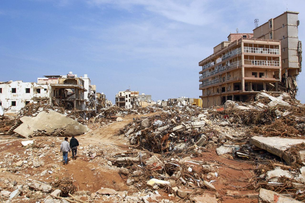 TOPSHOT - Men walk past debris of buildings caused by flash floods in Derna, eastern Libya, on September 11, 2023. Flash floods in eastern Libya killed more than 2,300 people in the Mediterranean coastal city of Derna alone, the emergency services of the Tripoli-based government said on September 12.