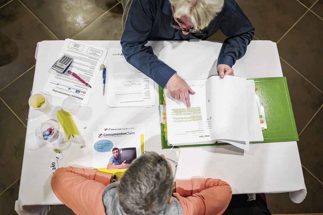 Een financieel adviseur kijkt een polis na, die een gedupeerde hem voorlegt tijdens de Nationale Ontwoekerdag in Utrecht in 2018. Bezoekers konden er gratis advies krijgen over hun woekerpolissen.