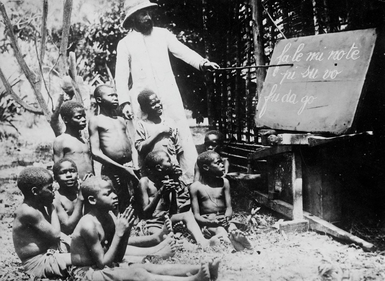 Missionaris in voormalig Belgisch Congo geeft leesles in de eigen taal aan de jezuïetenschool van Kwango, 1930.