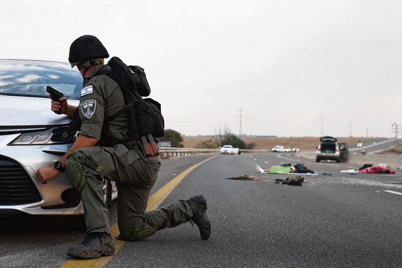 Een Israëlische militair zoekt zaterdag dekking bij een auto terwijl hij kijkt naar lichamen op een snelweg nabij de Gevim-kibboets, niet ver van de grens met Gaza.