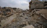 Syriërs lopen in een verwoeste straat in de wijk al-Arkoub, in Aleppo eind 2016.