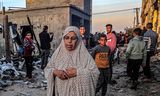 Een oudere vrouw loopt langs jongeren nabij gebouwen die zwaar zijn beschadigd door Israëlische bombardementen, zondag in Rafah in het zuiden van de Gazastrook.