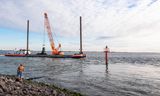 Een kraanschip werkt aan de versteviging van de oever bij de Vlissingse boulevard. De versterking bestaat uit staalslakken en stenen. 