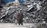 Een oudere man loopt met een kind aan de hand langs een gebouw in vluchtelingenkamp Bureij in Gaza dat door Israëlische bommen met de grond gelijk gemaakt is. 