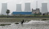 Een boer is aan het werk op zijn akker tegen de achtergrond van een koolcentrale in het Indiase Dadri, juni 2024. 