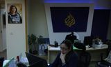 Een journalist van Al Jazeera aan het werk in het kantoor van de nieuwszender in Ramallah, op de Westelijke Jordaanoever, in mei 2023. Aan de muur hangt een portret van Al Jazeera-journalist Shireen Abu Akleh, die in 2022 werd doodgeschoten door een Israëlische soldaat op de bezette Westelijke Jordaanoever. 