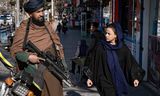 Een vrouw loopt langs een Taliban-strijder die op wacht staat in Kabul, december 2022.