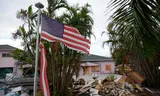 Een gescheurde Amerikaanse vlag wappert voor een huis, terwijl meubels die beschadigd zijn door de overstromingen van orkaan Helene opgestapeld langs de straat staan ​​te wachten tot ze worden opgehaald, ter voorbereiding op de komst van orkaan Milton, in Holmes Beach op Anna Maria Island, Florida, 8 oktober 2024.