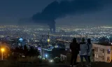 Rookwolken hangen boven Teheran na een Israëlische luchtaanval op 14 juni 2025. Op een nabijgelegen heuvel kijken mensen toe.