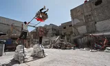 Een man duwt een jongen op een schommel in de door oorlog getroffen stad Douma, Syrië. Foto Omar Sanadiki 