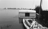 Wateroverlast door de hoge waterstand in de Maas in combinatie met mooi weer. Vrouw in bootje op ondergelopen camping.